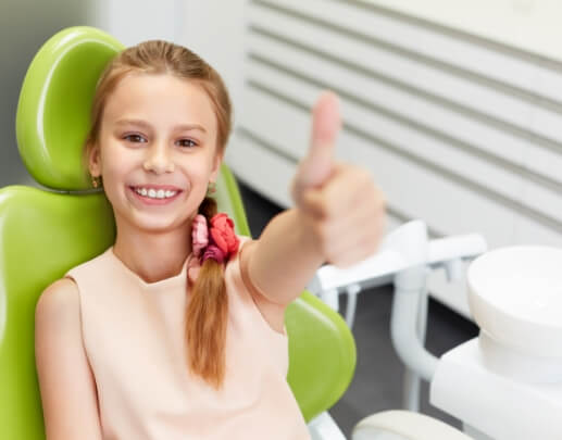 Child giving thumbs up after children's dental checkup and teeth cleaning