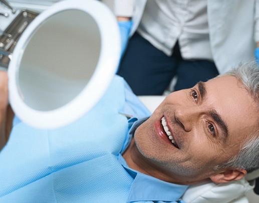 Man with veneers smiling at reflection in dentist's mirror